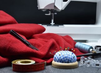 Jak zacząć szyć patchwork ręcznie i na maszynie – poradnik dla początkujących Czerwona tkanina przy maszynie do szycia i akcesoria do patchworku